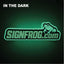 A glowing green and black SIGNFROG.com frog sign centered on a dark background, with the text 'IN THE DARK' in white at the top left.