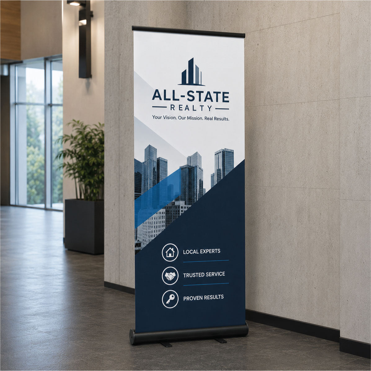 A vertical retractable banner stand displaying a real estate design with the text 'ALL-STATE REALTY' and city skyline graphics, placed in a modern indoor lobby with stone walls and windows.