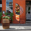 An orange promotional feather flag with food graphics standing on a brick sidewalk next to a storefront.⁠