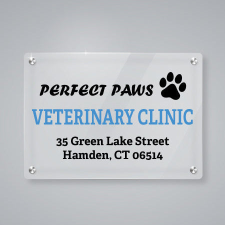 Clear custom acrylic business sign for Perfect Paws Veterinary Clinic featuring a black paw print logo and address details, mounted on a modern gray wall with silver standoffs.