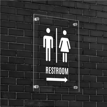 Clear acrylic restroom sign with white icons mounted on black brick wall.