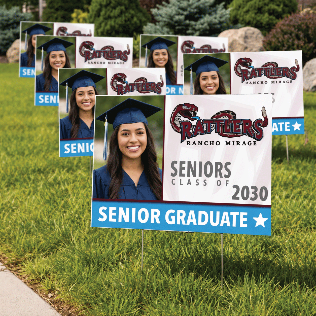 A large quantity of custom high school graduation yard signs displayed on a lawn, featuring senior graduate photo prints and Rancho Mirage Rattlers school spirit designs.