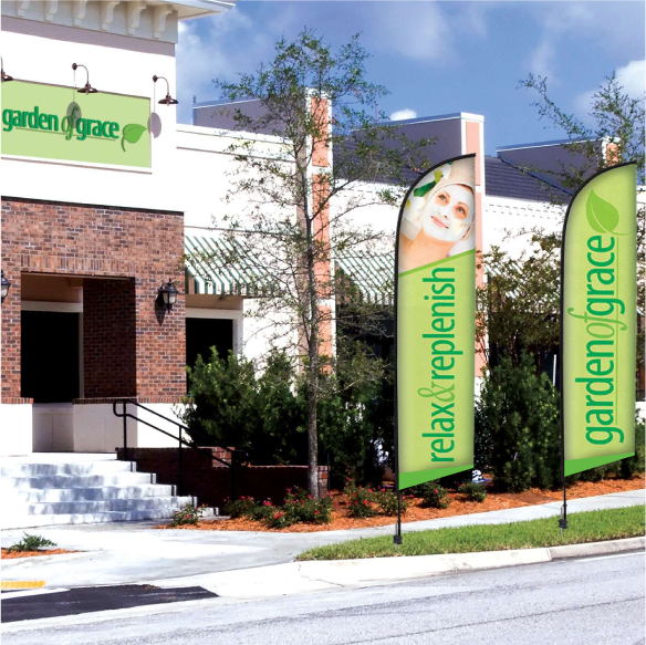 Custom green outdoor advertising flags for businesses mounted on a sidewalk landscape area.