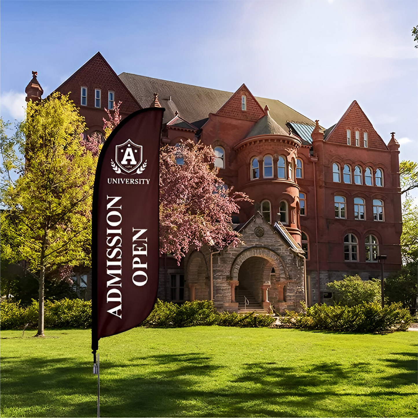 A maroon custom feather flag with "Admission Open" text standing on a green grass lawn in front of a brick campus building.⁠