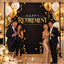 Two smiling couples celebrating in formal attire in front of a black and gold "Happy Retirement" step and repeat backdrop banner adorned with balloons.
