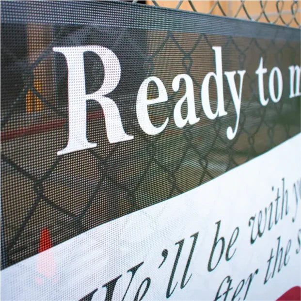 Close-up shot of a custom printed mesh banner attached to a metal fence, showing the clean text printing.⁠