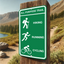 Green aluminum all-purpose trail sign for hiking, running, and cycling mounted on a wooden post in a park.
