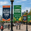 Custom outdoor boulevard pole banners for Bayside Town mounted on a black street lamppost, featuring a blue welcome banner with an anchor graphic and a green and yellow Summer Festival banner.