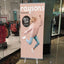 A pink custom pull-up advertising banner for a apparel store discount display standing inside a commercial shopping center corridor.⁠