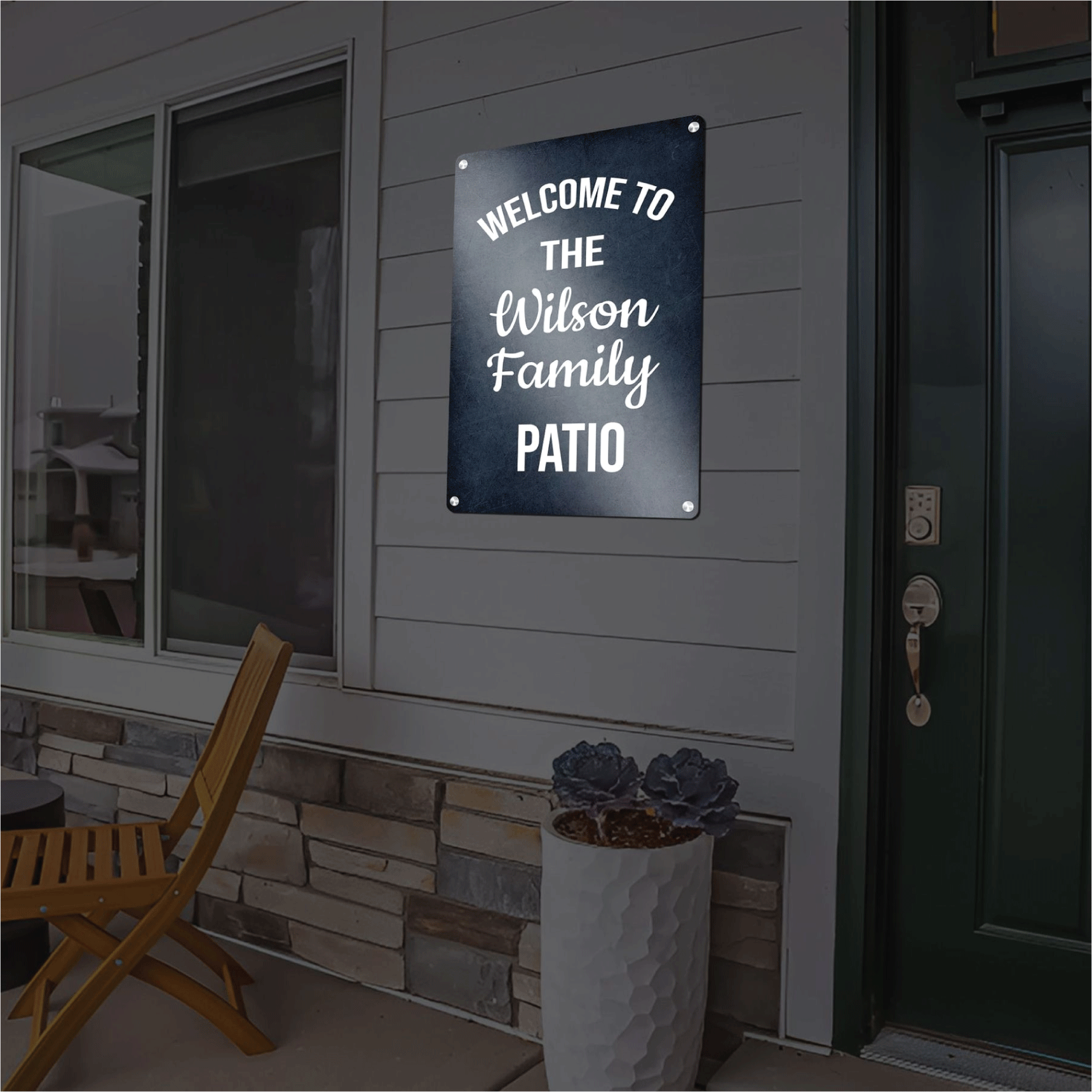 Custom dark blue reflective aluminum sign reading Welcome to the Wilson Family Patio in elegant white script, mounted outdoors on a home's siding next to a doorway.