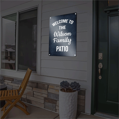 Custom dark blue reflective aluminum sign reading Welcome to the Wilson Family Patio in elegant white script, mounted outdoors on a home's siding next to a doorway.