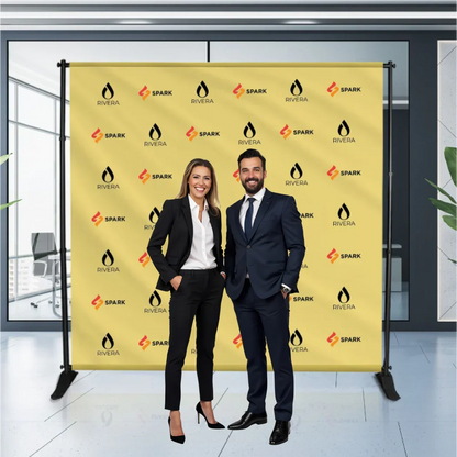 A professional man and woman posing in front of a yellow custom step and repeat logo backdrop banner at a corporate media event.⁠