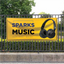 A bright yellow custom vinyl banner advertising a music store mounted to a black outdoor metal fence.⁠