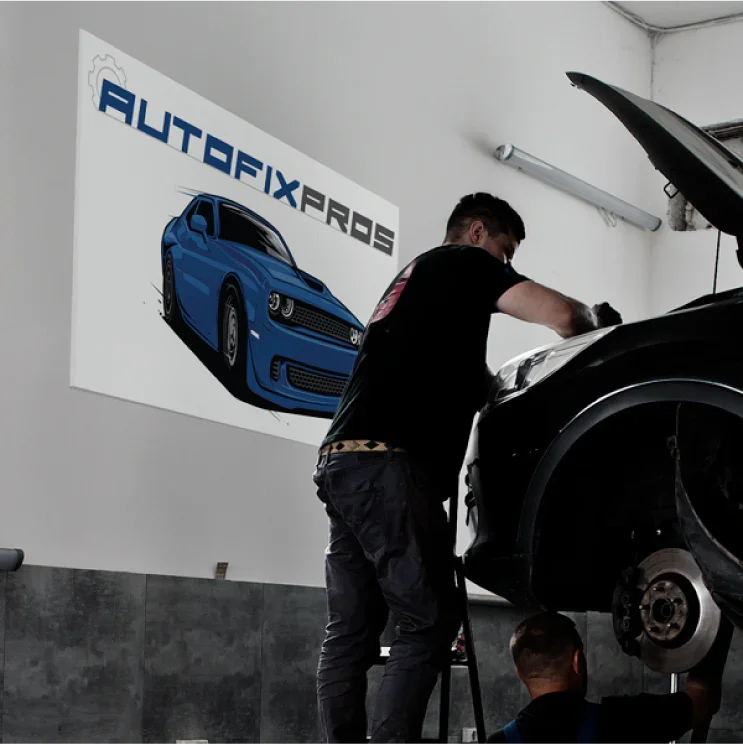 A large custom PVC board sign displaying an automotive logo on a garage wall above a mechanic working on a vehicle.⁠