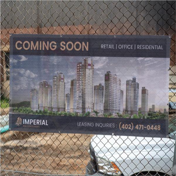 Large custom mesh fence banner featuring a "Coming Soon" real estate development graphic attached to a chain-link fence.