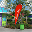 A bright red custom teardrop flag standing outside next to a green trash can with an amusement park ride background.⁠