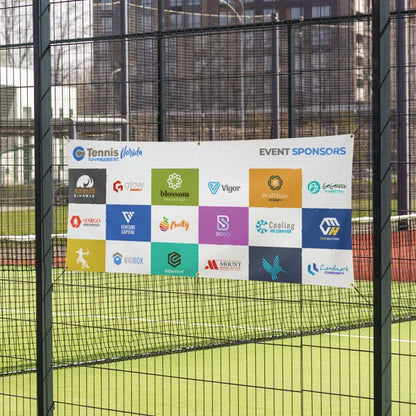A white multi-logo corporate sponsor vinyl banner attached cleanly to a chain-link sports field fence.⁠