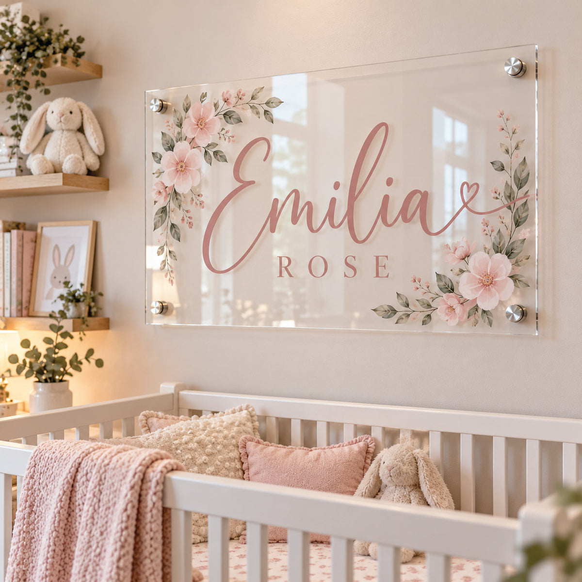 Custom clear acrylic nursery name sign featuring the name "Emilia Rose" in elegant pink lettering surrounded by delicate floral illustrations, mounted on a white wall above a baby crib.