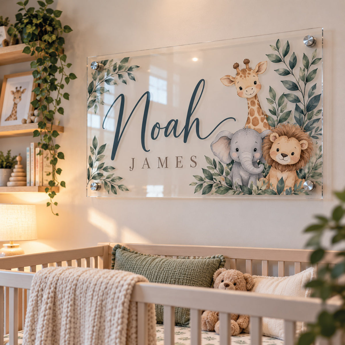 Custom clear acrylic nursery name sign featuring the name "Noah James" in bold navy typography surrounded by woodland safari illustrations including a cute giraffe, lion, and elephant, mounted on a white wall above a crib.