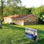A blue Just Listed real estate coroplast lawn sign standing on the grass field of a single-story ranch home.⁠