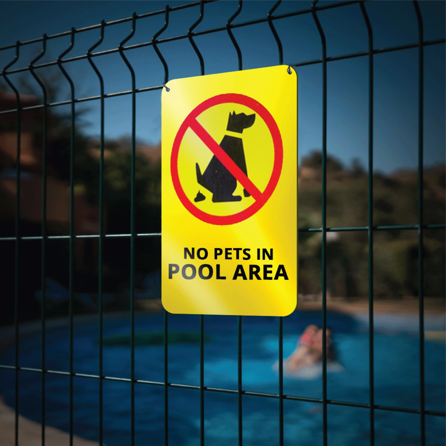 Custom yellow reflective aluminum safety sign with a black silhouette of a dog inside a red prohibition circle reading No Pets In Pool Area, mounted outdoors on a wire mesh fence with a swimming pool in the background.
