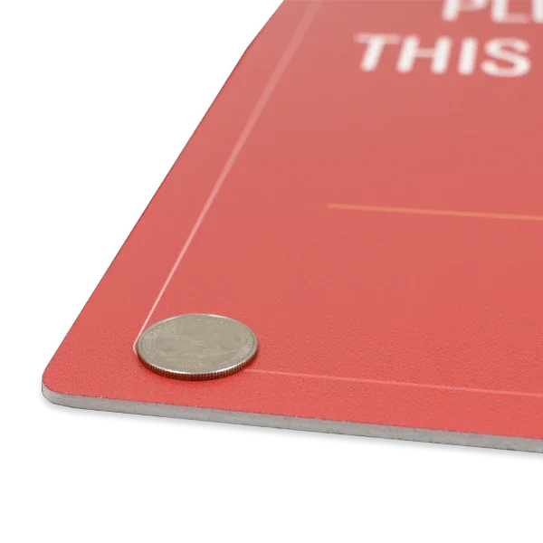 Close-up shot of a red rigid PVC plastic sign with a quarter placed on top to illustrate material thickness and durability.⁠