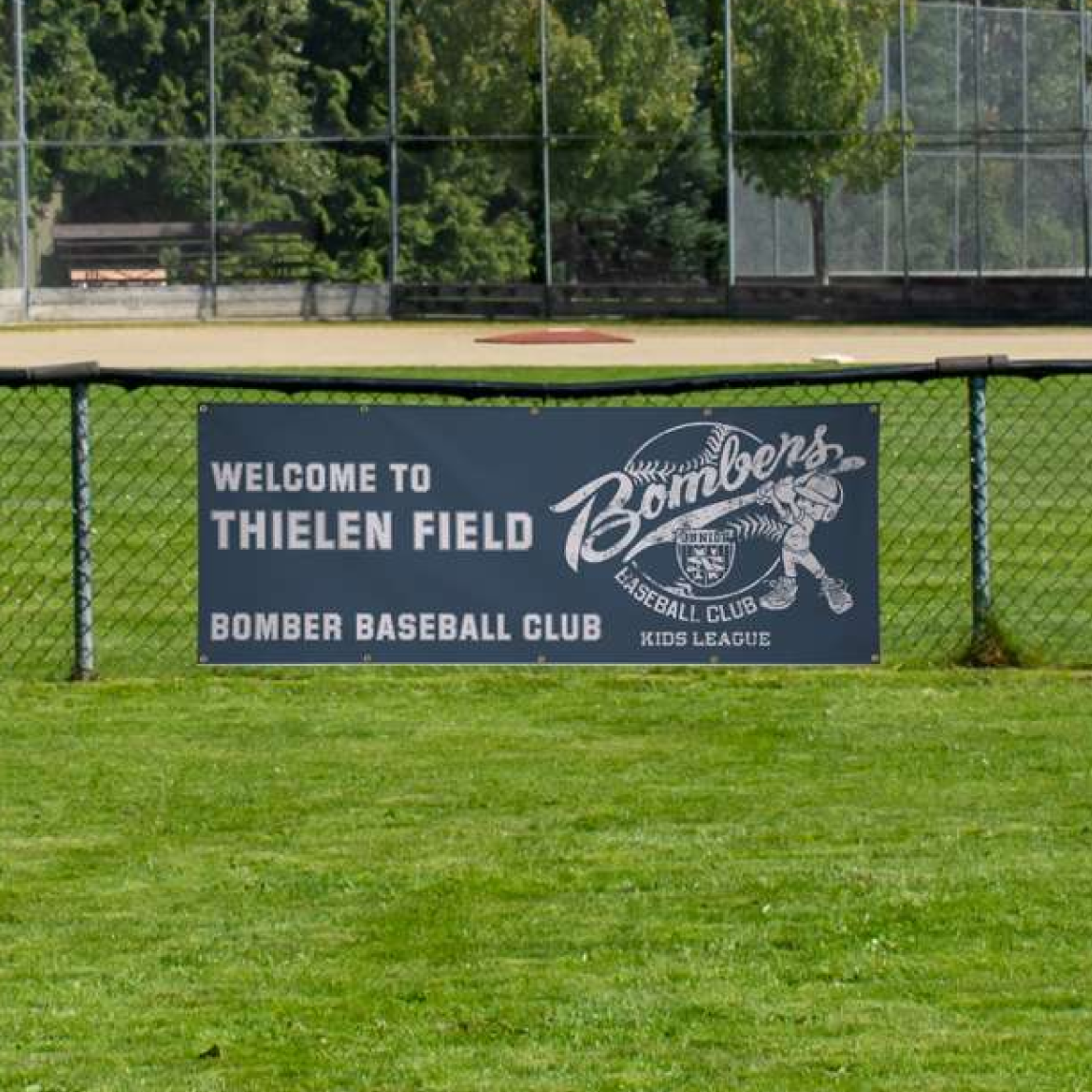 A blue custom sports sponsorship vinyl banner reading Welcome to Thielen Field mounted to an outfield baseball field fence.⁠