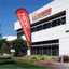 A bright red custom teardrop flag banner reading "NEW REWARD PROGRAM" standing outside a Trusted Credit Union building.
