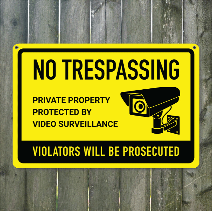 Yellow PVC plastic No Trespassing sign mounted on a wooden fence reading Private Property Protected by Video Surveillance.